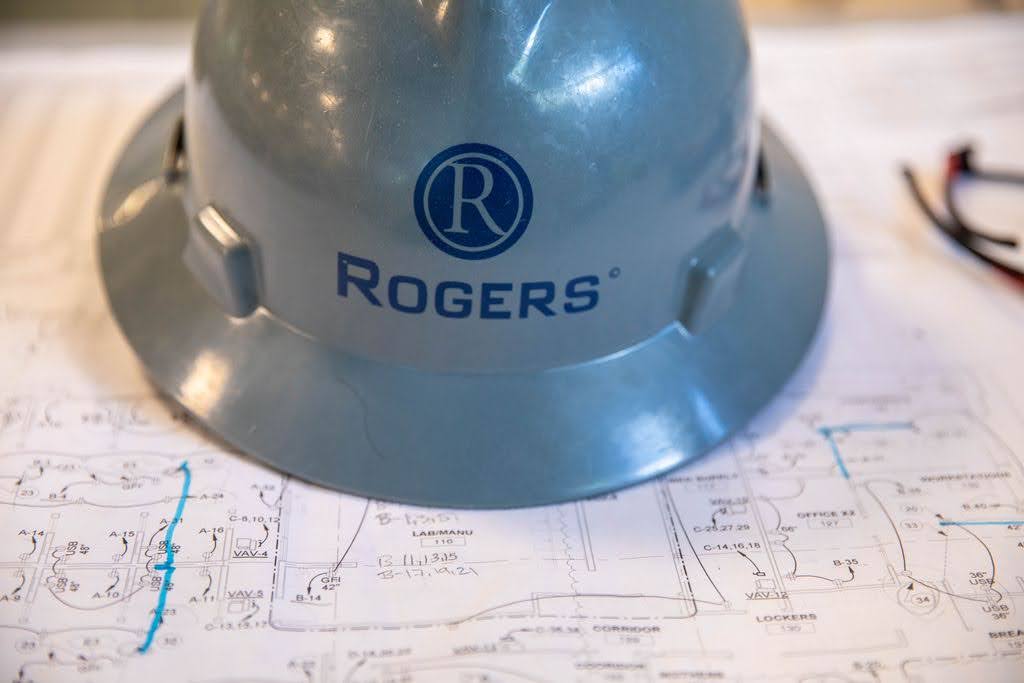 picture of gray hard hat that says Rogers Electric on top of a blueprint