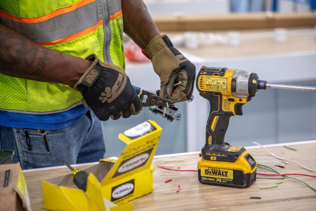 up-close shot of an electrician's hands working on electrical work and has a DeWalt drill