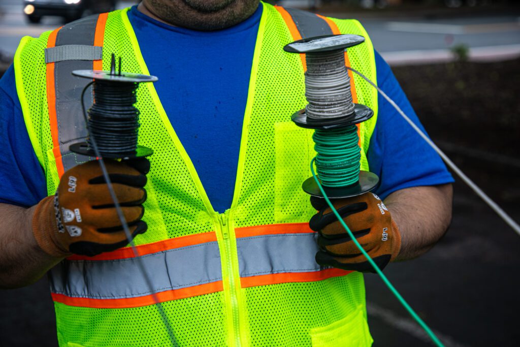 electrician's hands holding 3 spirals of electrical wire in hands- green, white, and black