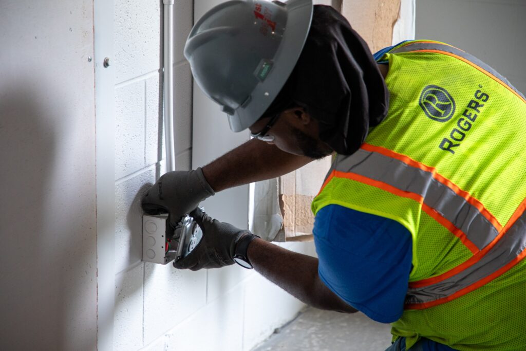 backside of electrician with Rogers safety vest and PPE gear installing an outlet