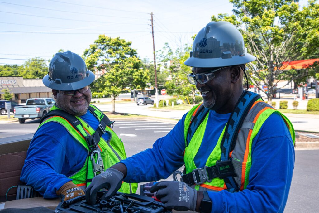 two electricians outside with all PPE gear on smiling while looking at electrical equipment